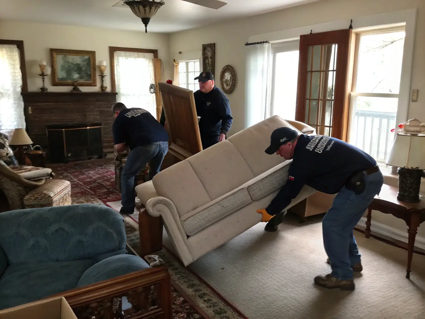 A Cowboy Junk Removal crew carrying a large sofa out of a house and loading it onto a truck, illustrating their furniture removal service.